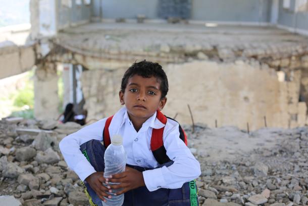 young boy in Yemen, looking sad, in front of his destroyed school