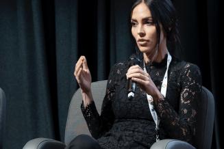 Picture of Natalie Kyriacou speaking at an event, sitting on a chair and holding a microphone