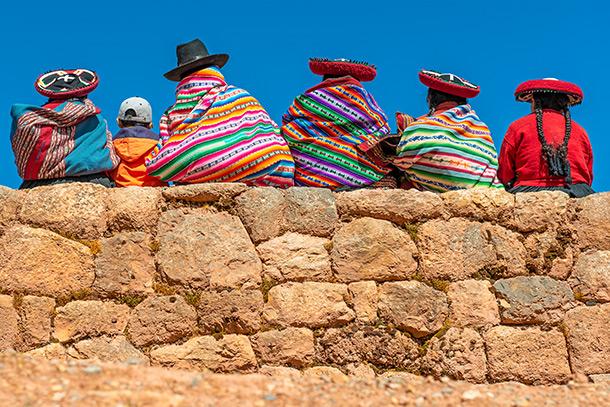 Un groupe de femmes indigènes Quechua en vêtements traditionnels et un jeune garçon assis et bavardant sur un ancien mur Inca dans le site archéologique de Chinchero dans la région de la ville de Cusco, Pérou