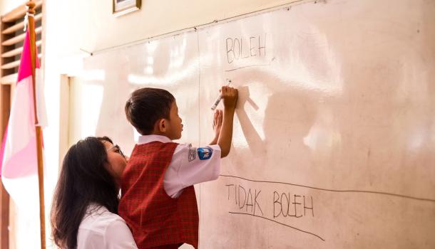 a teacher guiding a student to write in Indonesia